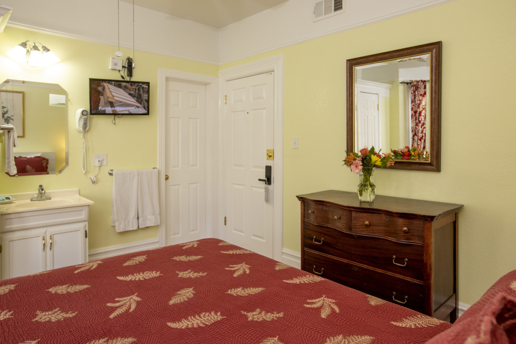 A wide view of a hotel room with a red bedspread, yellow walls, and white furniture.