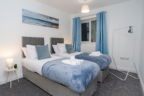 Stylish blue twin room with two comfortable beds, dressed in crisp fresh linens and complete with soft towels — a modern, relaxing space for a great night’s sleep.
