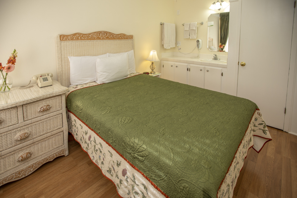 A hotel room with a bed, dresser, and sink area