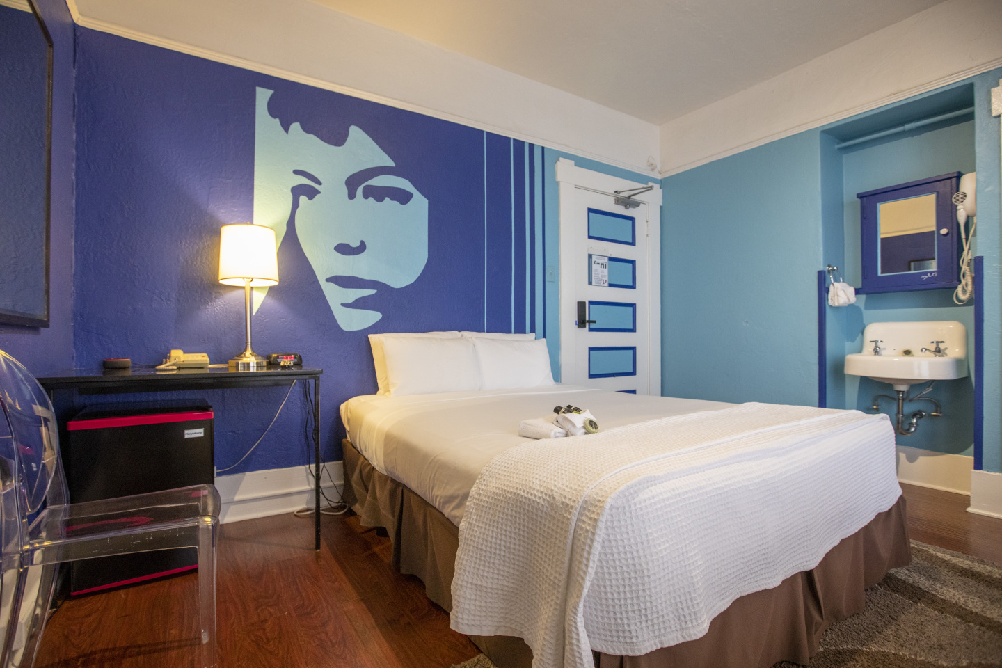 A hotel room with a single bed, desk, sink, and television.