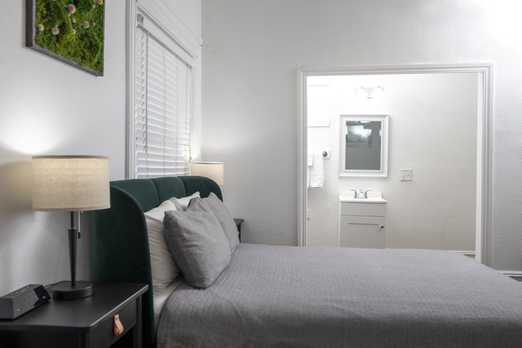 A hotel room with a bed, nightstand, lamp, window, and bathroom doorway.