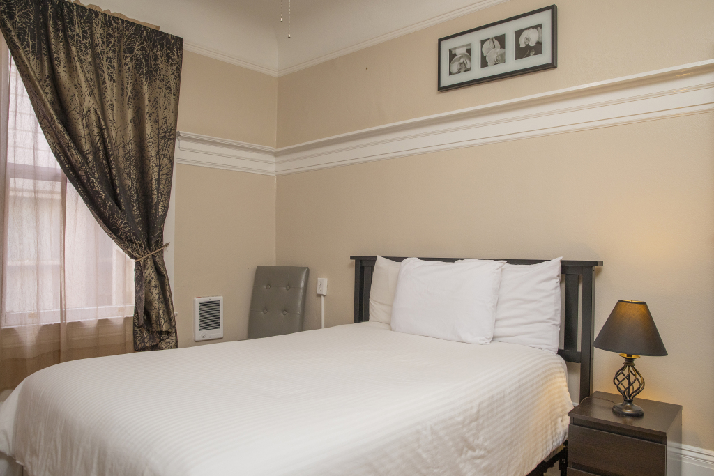 A hotel room with a large bed, nightstand, and window.