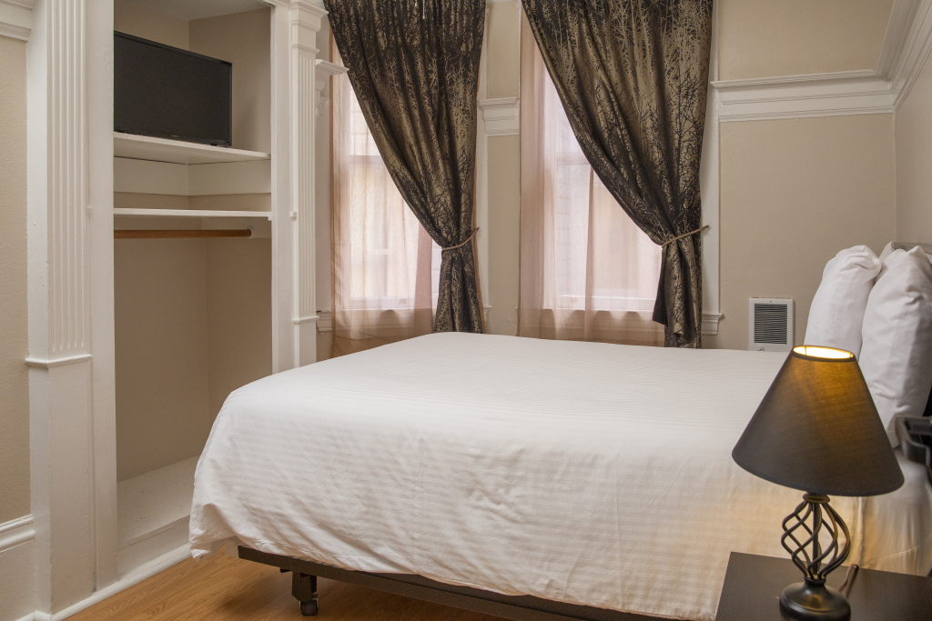 A hotel room with a bed, lamp, closet, and window