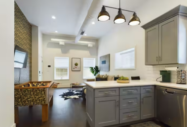 This open-concept kitchen flows seamlessly into the living area, with elegant grey cabinets, industrial-style pendant lighting, & a convenient coffee maker. The design creates a welcoming, connected space perfect for cooking & entertaining guests.