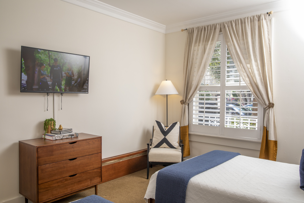 A hotel room with a bed, dresser, chair, lamp, and TV on the wall.