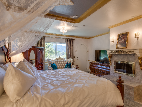Palace Suite King bed adorned with delicate, lace curtains with center view of wood-burning fireplace.